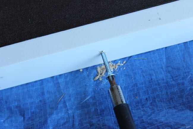 Carefully drill the screw through the frame and canvas