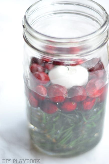 Combine the greenery, cranberries, floating candle and water in the mason jar. 