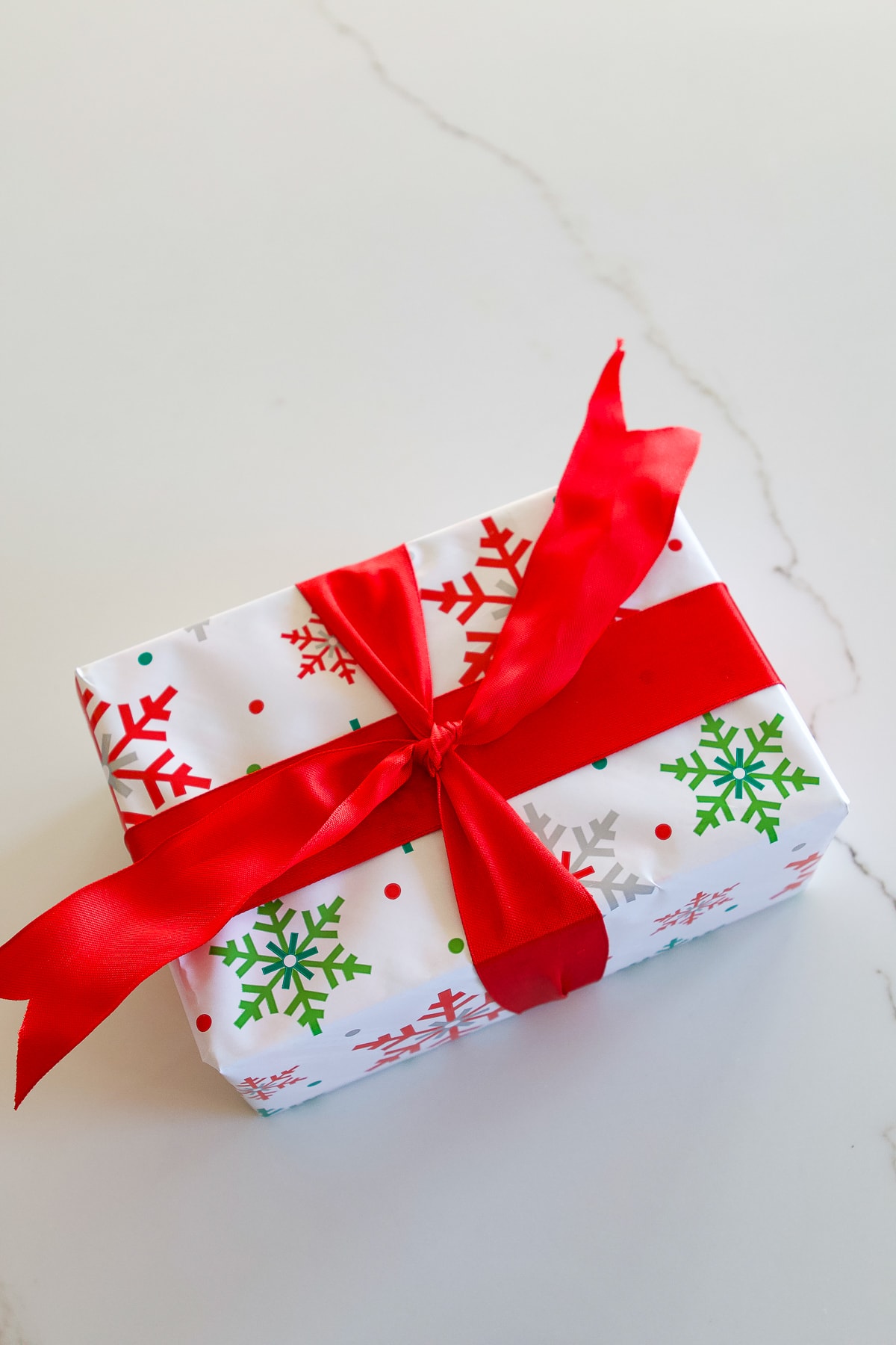 Gift box wrapped in craft paper, ribbon, bow and scissors on white