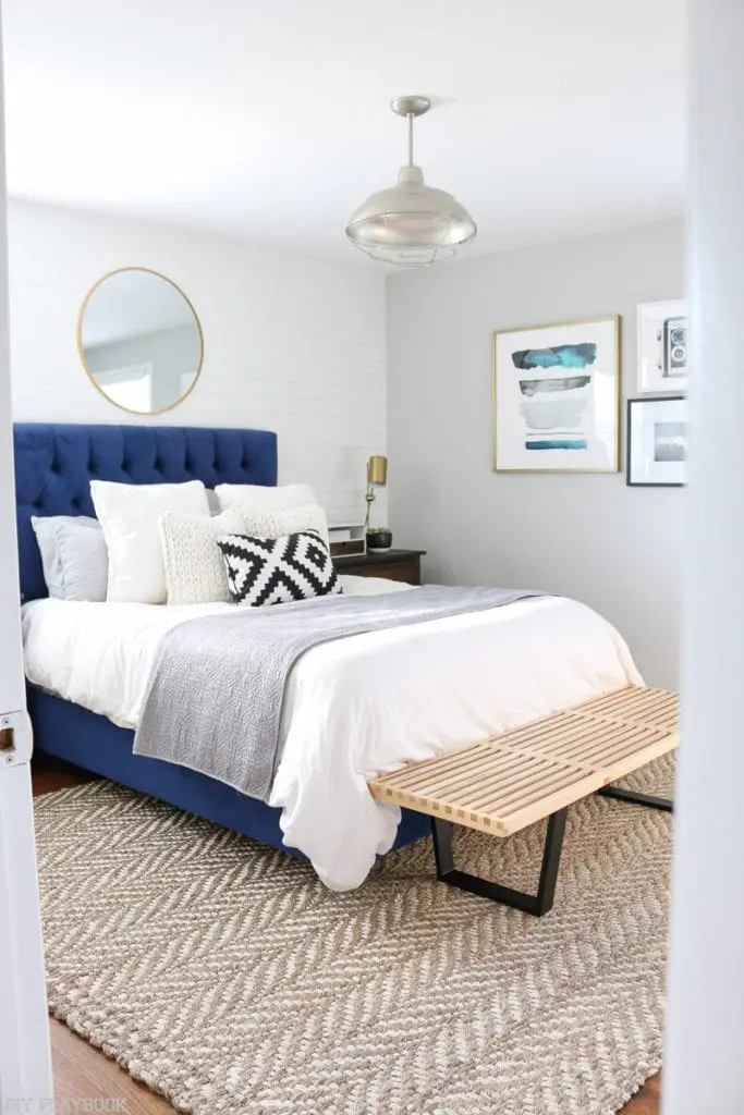 Bedroom with herringbone rug, white pillows and bright blue headboard. 