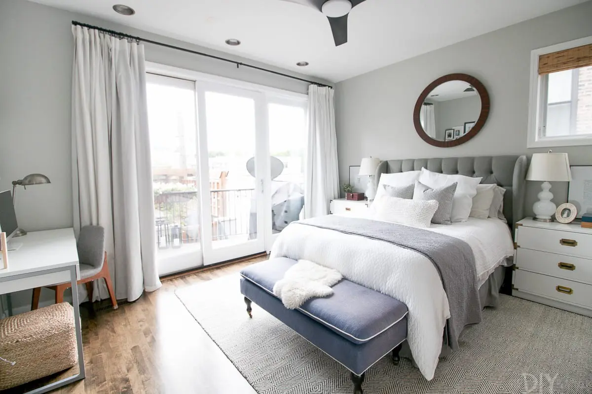 Soft grey bedroom with a white comforter, white furniture and pop of blue at the foot of the bed. 