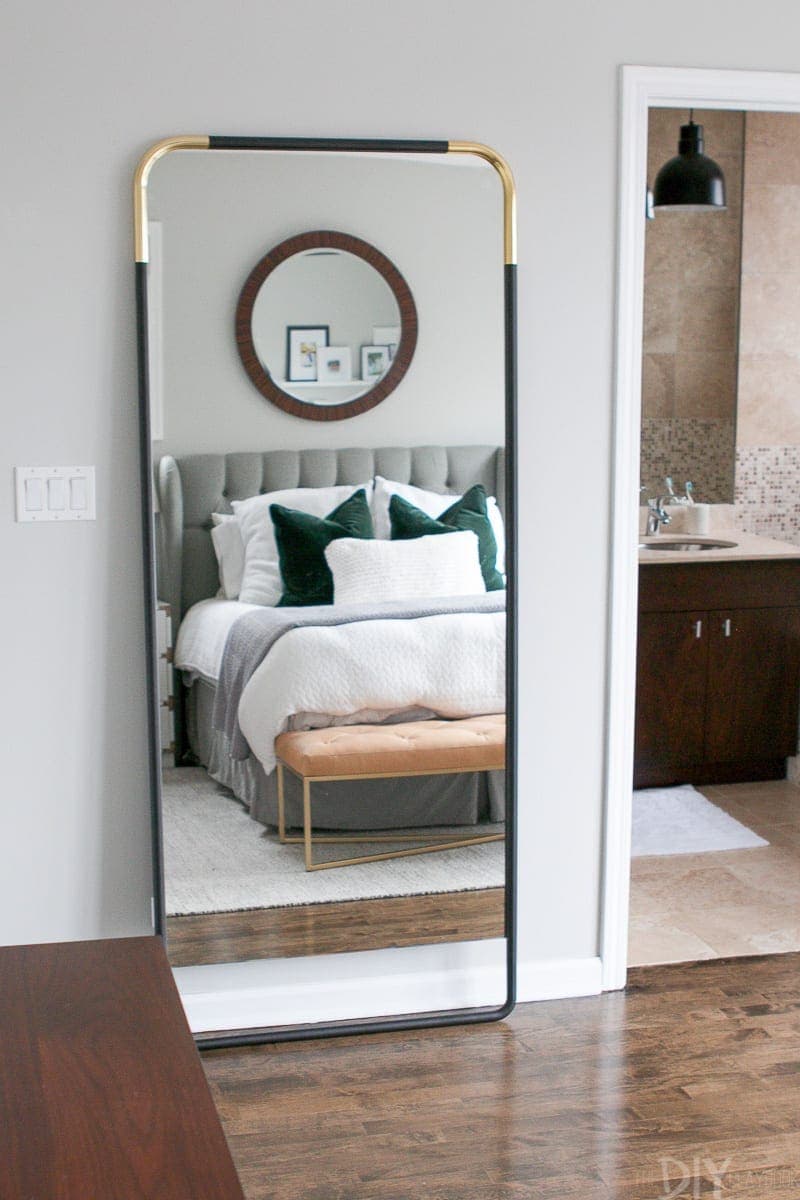 A black and brass mirror that is secured to the wall using furniture straps. 