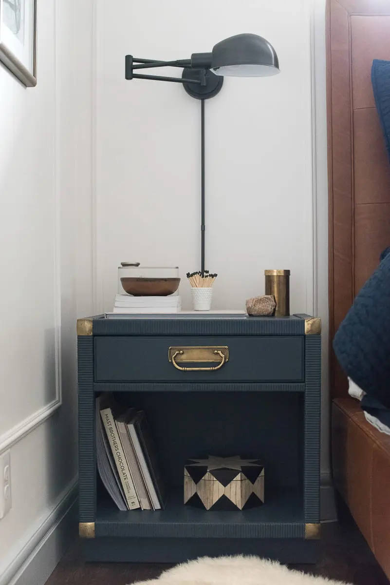 DIY nightstand painted navy with a black sconce hanging over it. 