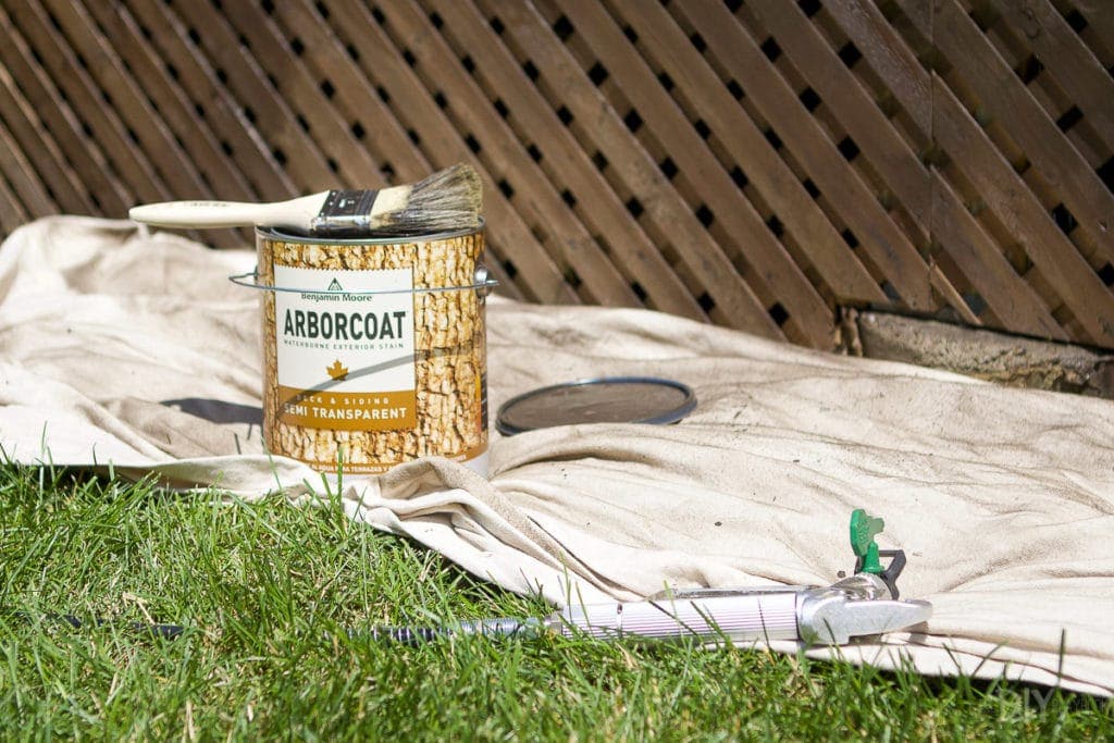 Using a paint sprayer and brush to stain a deck