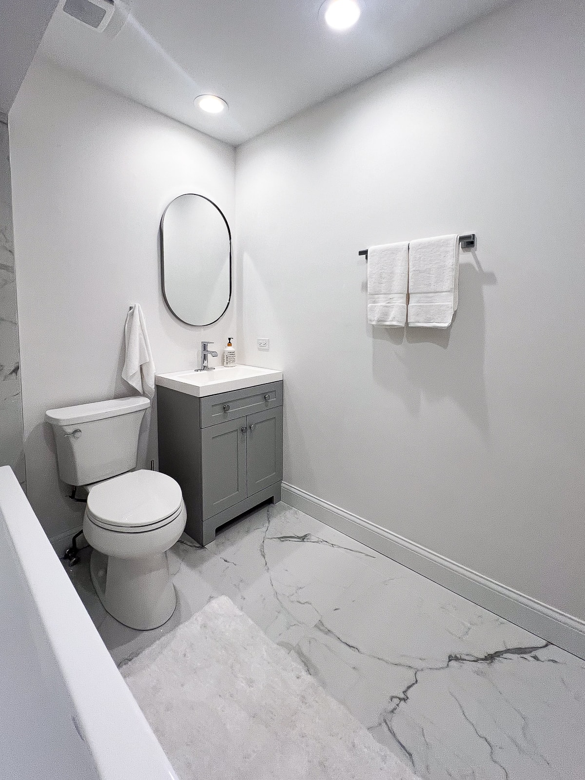 Une salle de bain entièrement blanche avec de la peinture blanche, des sols en marbre et une vanité grise